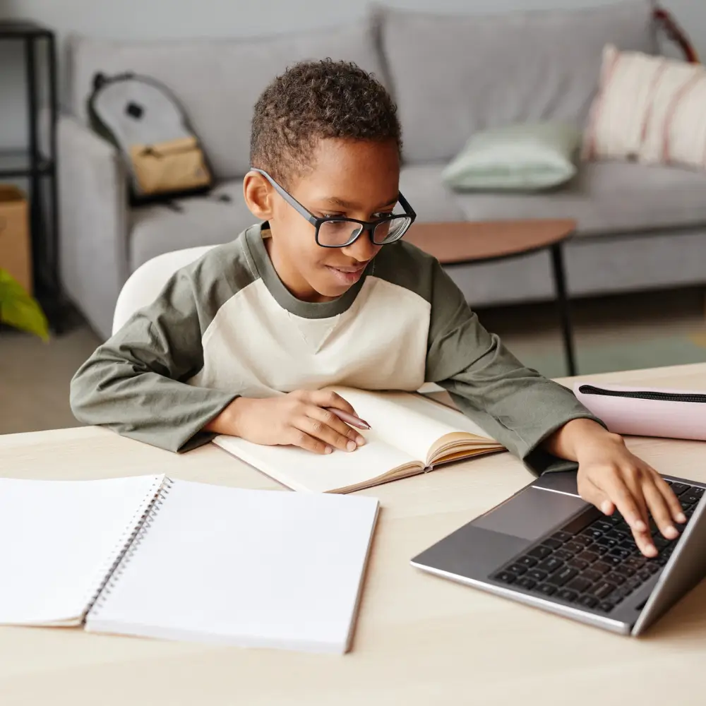 Image of smiling African American boy wearing glasses using laptop while studying at home homeschooling concept copy space
