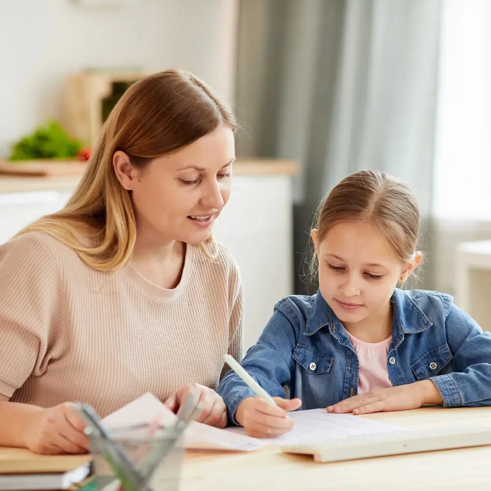 caring mother helping cute girl doing homework and studying at home in cozy interior